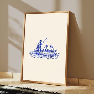 Puede incluir: Una l&aacute;mina de arte enmarcada con una ilustraci&oacute;n en tinta azul sobre fondo crema. La obra representa a tres figuras en un peque&ntilde;o bote de remos sobre el agua, con una persona de pie usando un remo mientras otras dos est&aacute;n sentadas en el bote.
