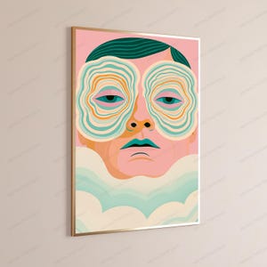 May include: A framed wall art print featuring a stylized human face with dark teal hair. The eyes are surrounded by concentric, wavy orange and teal circular patterns. The lips are teal, and the lower portion of the face is obscured by soft, light-colored clouds.