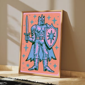 May include: A framed art print featuring a stylized illustration of a knight in armor, holding a sword and a shield with a star emblem. The knight is rendered in shades of blue and pink against a solid peach background, surrounded by blue stars.