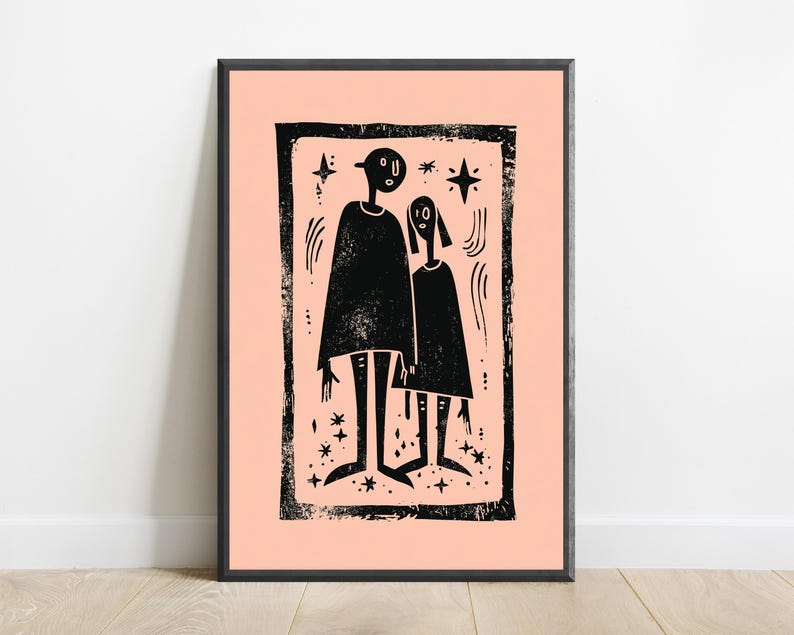 May include: A framed wall art print featuring a black ink block print illustration of two stylized figures standing side by side on a light peach background. The artwork includes small star shapes and curved lines, all enclosed within a textured black border.
