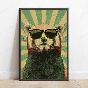 May include: A framed wall art print featuring a red panda wearing black sunglasses. The animal is centered against a background of radiating green and beige sunburst lines. The illustration uses a textured, vintage-inspired graphic style.