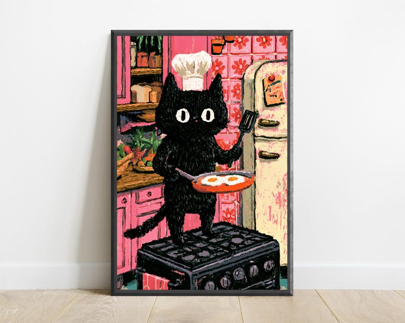 Peut inclure: Une impression d'art encadr&eacute;e repr&eacute;sentant un chat noir portant une toque de chef blanche, debout sur une cuisini&egrave;re noire dans une cuisine rose. Le chat tient une spatule noire et une po&ecirc;le rouge contenant deux &oelig;ufs au plat, devant des meubles roses.