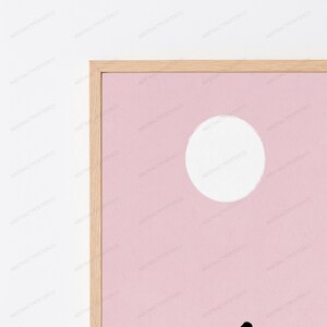 May include: A framed wall art print featuring a solid light pink background with a large white circle positioned in the upper right quadrant. The frame is constructed from light-toned wood with a visible grain, surrounding the rectangular print.