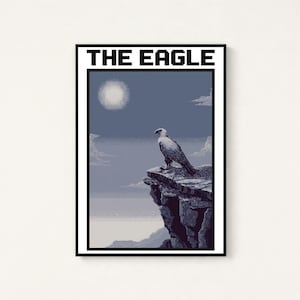 May include: A rectangular wall art print featuring a pixel art style eagle perched on a rocky cliff edge. The scene includes a pale sun in a blue sky with clouds and the text THE EAGLE printed in bold black capital letters at the top.