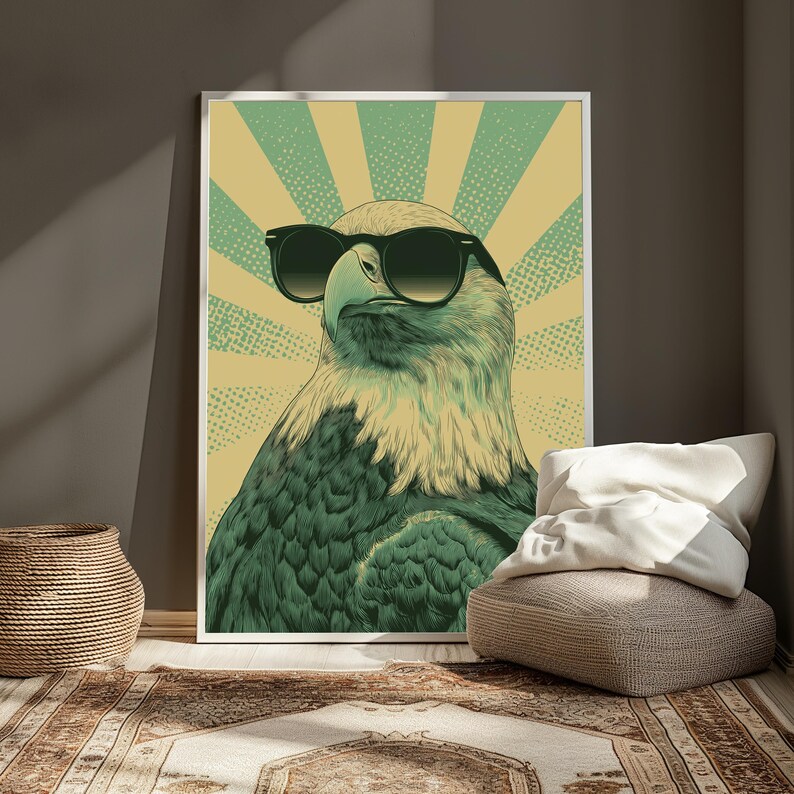 May include: A framed wall art print featuring a stylized illustration of a bald eagle wearing black sunglasses. The eagle is centered against a background of alternating light yellow and muted green sunburst rays with a subtle dotted texture.
