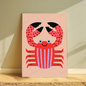May include: A rectangular wall art print featuring a stylized crab illustration on a light peach background. The crab has a red body with vertical purple stripes, two large pink claws with red spots and black tips, and six red legs. It has two blue eyes.