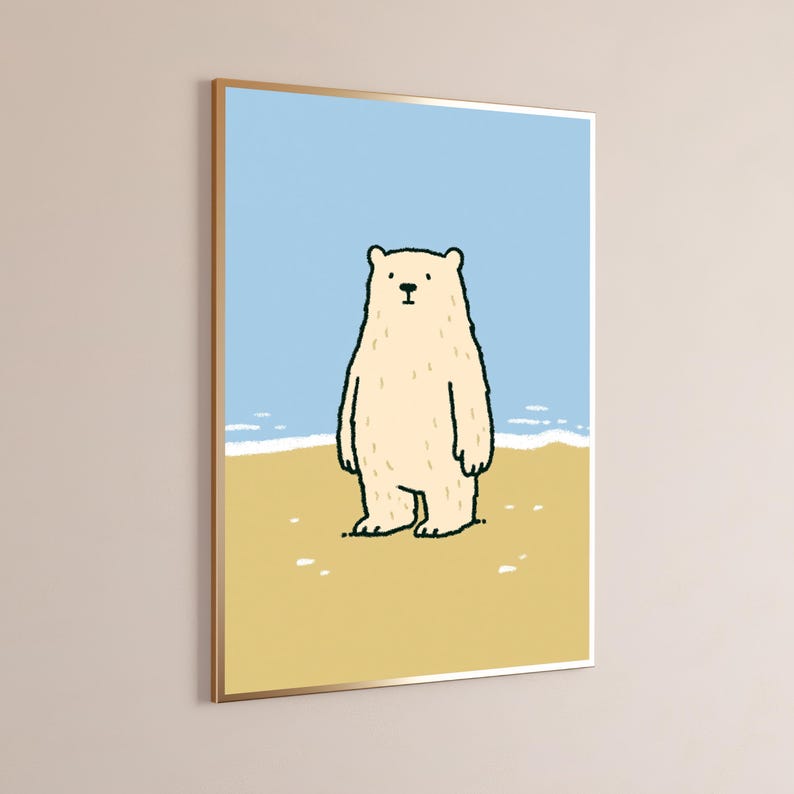 May include: A framed wall art print featuring a cartoon illustration of a cream-colored bear standing on a tan sandy beach. The background shows a light blue sky and a thin white line representing the ocean waves meeting the shore.