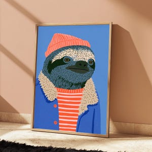 May include: A framed art print featuring a stylized illustration of a sloth wearing a coral-colored beanie, a red and white striped shirt, and a blue jacket with a beige faux-fur collar, all set against a solid light blue background.