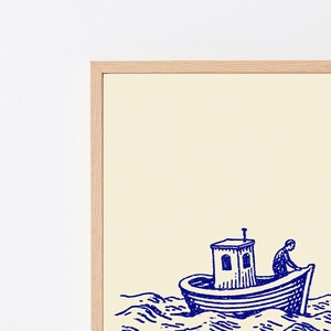 May include: A framed wall art print featuring a dark blue ink illustration of a small boat with a cabin on choppy water. A figure is visible on the deck of the boat. The print is set against a light cream background and enclosed in a light wood frame.