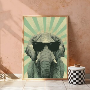 May include: A framed wall art print featuring a detailed illustration of an elephant wearing black sunglasses. The elephant is centred against a light green background with a radiating sunburst pattern in a darker shade of green.
