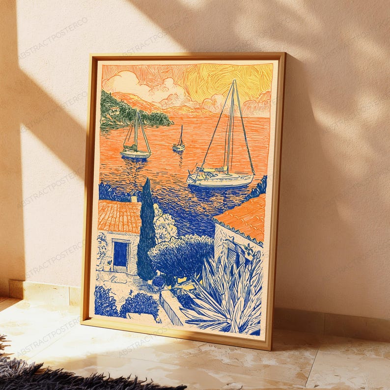 May include: A framed art print featuring a coastal scene with sailboats on a vibrant orange sea. The foreground shows blue-toned houses with terracotta roofs, lush vegetation, and a large agave plant, all rendered in a detailed, sketch-like style.