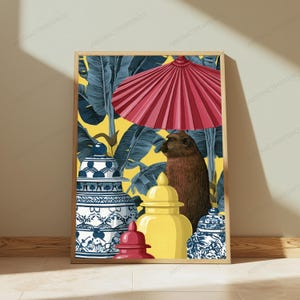 May include: A framed art print featuring a brown monkey standing beneath a large red parasol. The scene includes two blue and white patterned ginger jars and a solid yellow ginger jar, all set against a background of dark blue banana leaves.