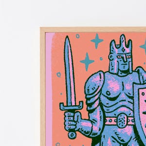 May include: A framed art print featuring a stylized illustration of a knight in blue armor holding a sword and shield. The background is a solid peach color with blue star shapes. The knight wears a crown and has a textured, graphic appearance.