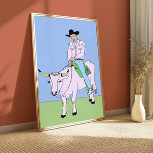 May include: A framed art print featuring a line-art illustration of a person wearing a black cowboy hat, a light pink button-down shirt, and blue jeans, riding a light pink cow with green saddle gear against a light blue and green background.