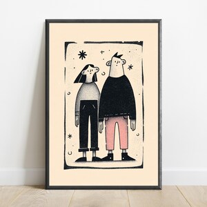 May include: A framed art print featuring a stylised illustration of two figures standing side by side. The figure on the left wears a grey top and black trousers, while the figure on the right wears a black top and pink trousers, all set against a cream background.