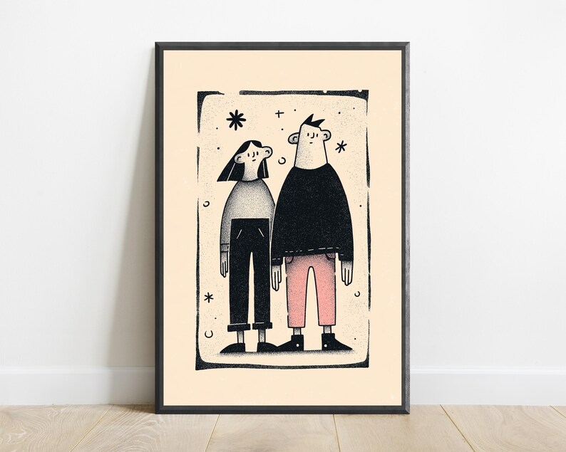 May include: A framed art print featuring a stylised illustration of two figures standing side by side. The figure on the left wears a grey top and black trousers, while the figure on the right wears a black top and pink trousers, all set against a cream background.