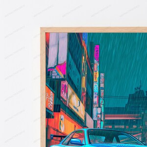 May include: A framed wall art print depicting a rainy city street scene at night with a blue sports car in the foreground. The image features vibrant neon signs with Japanese text, tall buildings, and a teal-toned sky, all encased in a light wood frame.
