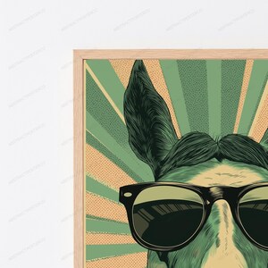 May include: A framed wall art print featuring a stylized illustration of a donkey wearing black sunglasses. The background consists of alternating green and tan sunburst rays with a dotted texture, all encased in a light wood frame.