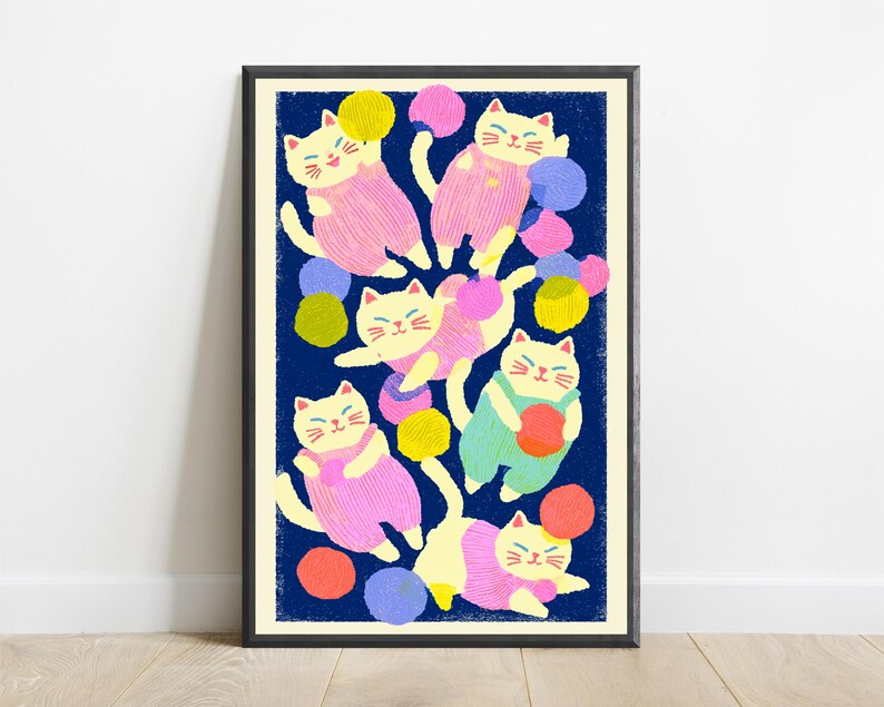 May include: A framed art print featuring a dark blue background with multiple cream-colored cats wearing pink, green, and yellow overalls. The cats are depicted playing with various colorful yarn balls in shades of pink, yellow, orange, and blue.