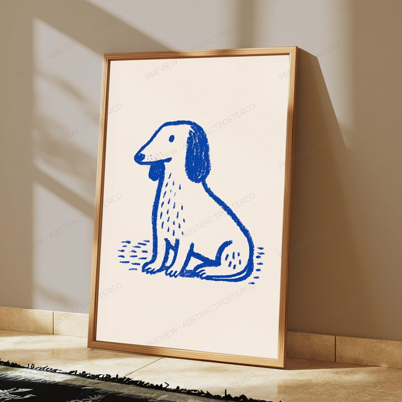 K&ouml;nnte beinhalten: Ein gerahmter Wandkunstdruck mit einer blauen Buntstiftzeichnung eines sitzenden Dackels auf cremefarbenem Hintergrund. Der Hund hat einen langen K&ouml;rper, Schlappohren und eine einfache Kontur. Der Rahmen ist d&uuml;nn und metallisch goldfarben.