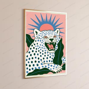 May include: A rectangular wall art print in a gold frame featuring a white leopard with blue spots and an open mouth. The leopard is surrounded by dark green leaves against a pink background with a blue sunburst design positioned behind its head.