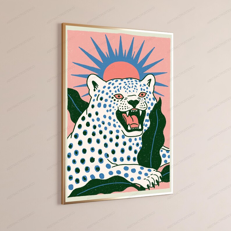 May include: A rectangular wall art print in a gold frame featuring a white leopard with blue spots and an open mouth. The leopard is surrounded by dark green leaves against a pink background with a blue sunburst design positioned behind its head.