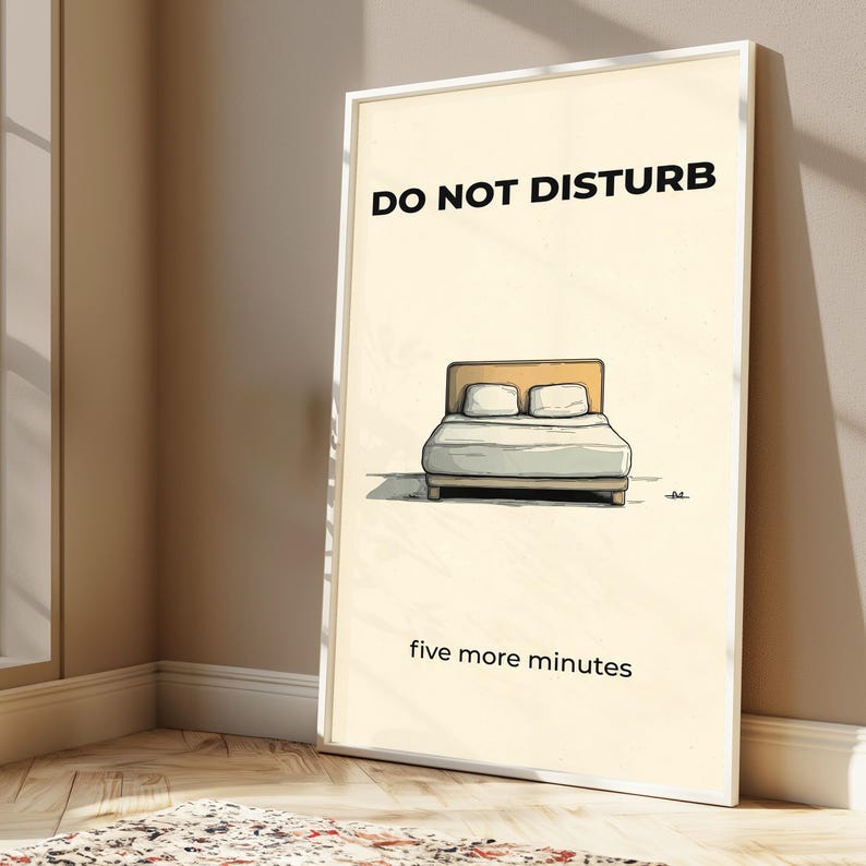 Puede incluir: Un cuadro enmarcado con las palabras "DO NOT DISTURB" sobre una ilustraci&oacute;n de una cama. Debajo de la cama, el texto dice "five more minutes". La obra de arte tiene un estilo minimalista con un fondo crema.