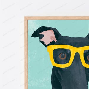 K&ouml;nnte beinhalten: Ein gerahmter Wandkunstdruck mit einer Nahaufnahme eines schwarzen Hundes, der eine leuchtend gelbe Brille vor einem strukturierten hellblauen Hintergrund tr&auml;gt. Der Hund hat ein sichtbares Ohr mit rosa Innenseite und dunkelbraune Augen.
