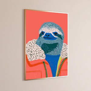 May include: A framed wall art print featuring a stylized illustration of a sloth with blue fur wearing a bright coral jacket with a white faux-fur collar over a blue sweater, set against a solid coral background with a thin gold frame.