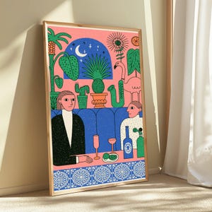 May include: A framed art print featuring a stylized illustration of two figures sitting in a blue booth. The scene includes a pink background, potted cacti, a flamingo, a crescent moon, and a table with glasses, a bottle, and a plate of limes.