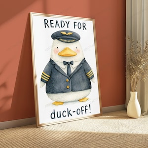 May include: A framed wall art print featuring a watercolor illustration of a white duck dressed as a pilot in a navy blue uniform with gold stripes, a black tie, and a pilot cap. The text reads READY FOR at the top and duck-off! at the bottom.