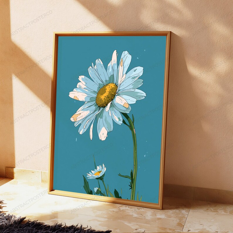 May include: A framed vertical art print featuring a large white daisy with a textured yellow center against a solid teal blue background. A smaller daisy bud is visible at the bottom left. The artwork is enclosed in a thin light wood frame.