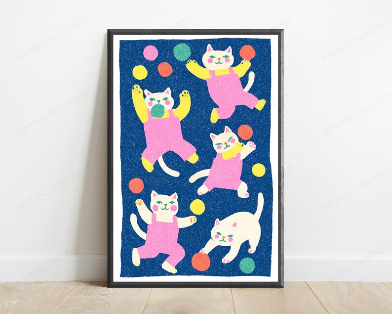K&ouml;nnte beinhalten: Ein gerahmter Kunstdruck mit f&uuml;nf wei&szlig;en Katzen in rosa Latzhosen vor einem texturierten dunkelblauen Hintergrund. Die Katzen sind in verschiedenen verspielten Posen dargestellt, umgeben von verstreuten bunten Kreisen in Gelb, Orange, Pink und Gr&uuml;n.
