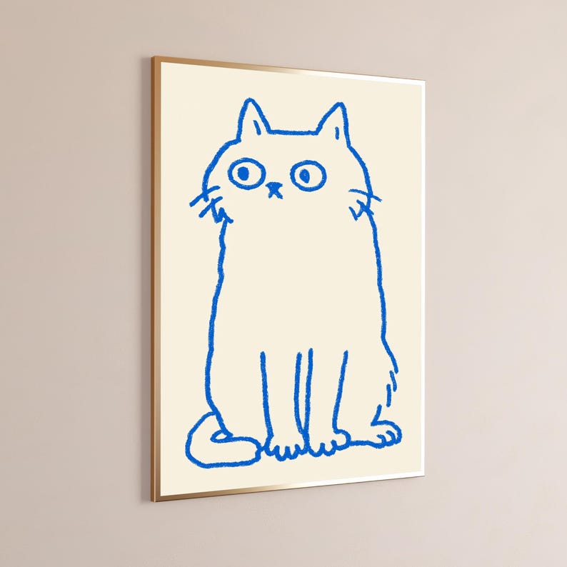 May include: A framed wall art print featuring a simple, hand-drawn style illustration of a cat in vibrant blue ink. The cat is depicted with wide, circular eyes and a small nose, set against a solid, light cream-colored background.