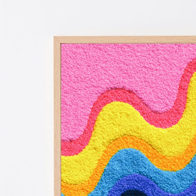 May include: A framed wall art piece featuring a textured, tufted surface with horizontal wavy bands of color. The design displays vibrant layers of pink, yellow, orange, and blue, creating a tactile, rippled effect within a light wood frame.