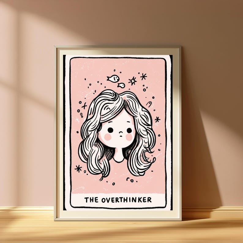 May include: A framed art print featuring a pale pink background with a black-outlined illustration of a person with wavy hair, rosy cheeks, and small fish and star icons floating above. The text THE OVERTHINKER is printed in black at the bottom.