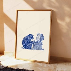 May include: A vertical rectangular framed print featuring a blue ink-style illustration of a chimpanzee sitting at a vintage computer desk. The primate is depicted typing on a keyboard with a monitor and tower unit, set against a plain cream background.