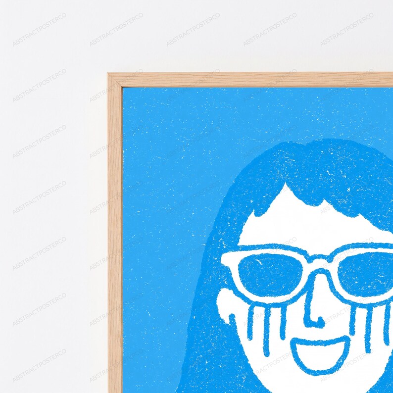 May include: A framed wall art print featuring a bright blue background with a white graphic illustration of a face wearing sunglasses. The figure has long hair and vertical lines extending downward from the sunglasses, framed in a light wood border.