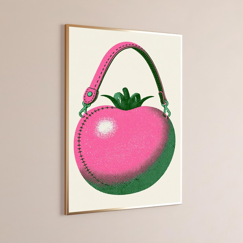 May include: A framed wall art print featuring a stylized illustration of a pink tomato-shaped handbag with a green stem top. The bag has a pink strap with green edges, dark green shading, and visible stitching details in a halftone dot pattern.