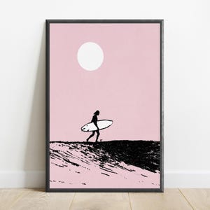 K&ouml;nnte beinhalten: Ein gerahmter Wandkunstdruck mit der schwarzen Silhouette einer Person, die ein Surfbrett &uuml;ber eine texturierte schwarze Welle tr&auml;gt, vor einem einfarbigen hellrosa Hintergrund mit einer wei&szlig;en kreisf&ouml;rmigen Sonne in der oberen Mitte.