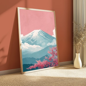 May include: A framed art print depicting a mountain landscape with a pink sky, snow-capped mountain, and blue hills. Pink cherry blossoms are in the foreground. The frame is gold-colored. The artwork is leaning against a red-orange wall.