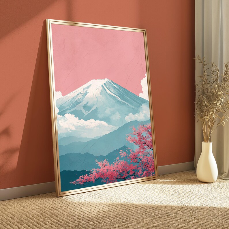 May include: A framed art print depicting a mountain landscape with a pink sky, snow-capped mountain, and blue hills. Pink cherry blossoms are in the foreground. The frame is gold-colored. The artwork is leaning against a red-orange wall.