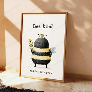 K&ouml;nnte beinhalten: Ein gerahmter Kunstdruck mit einer flauschigen, schwarz-gelb gestreiften Bienenfigur, die eine kleine gelbe Blume h&auml;lt. Die Biene tr&auml;gt einen winzigen Blumentopf auf dem Kopf. Der Text lautet oben Bee kind und unten and let love grow.