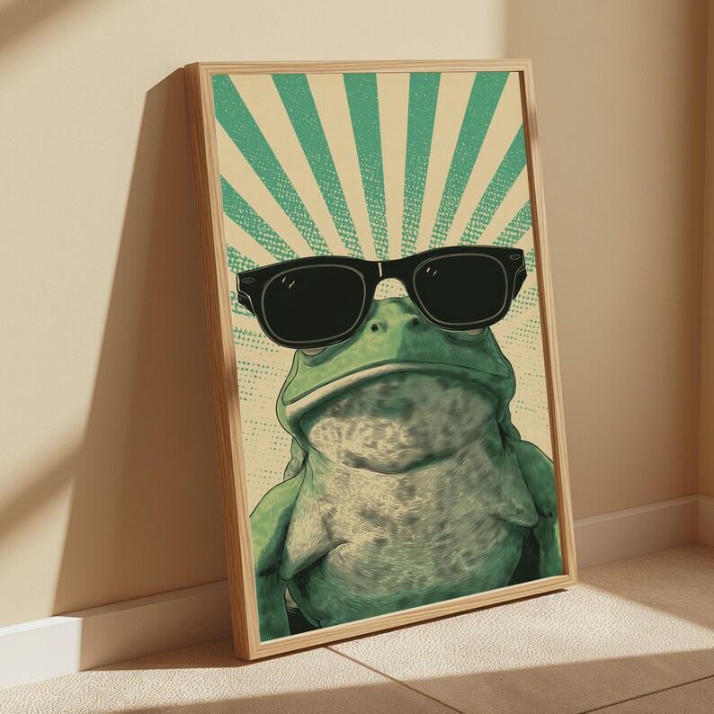 K&ouml;nnte beinhalten: Ein gerahmter vertikaler Wandkunstdruck, der einen gr&uuml;nen Frosch mit einer gro&szlig;en schwarzen Sonnenbrille zeigt. Der Hintergrund besteht aus einem cremefarbenen Feld mit strahlenden t&uuml;rkisen Sonnenstrahlen und einem Punktmuster, in einem hellen Holzrahmen.