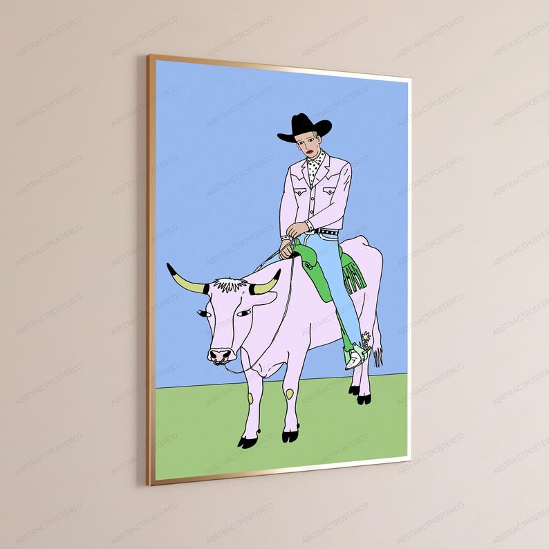 May include: A framed wall art print featuring a line drawing of a person in a black cowboy hat, pink jacket, and blue jeans riding a light pink bull. The bull has yellow horns and stands on a green field against a light blue sky background.