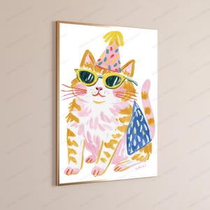 K&ouml;nnte beinhalten: Ein gerahmter Wandkunstdruck mit einer malerischen Illustration einer orangefarbenen getigerten Katze, die einen bunten Partyhut mit rosa und gelben Punkten, eine gr&uuml;ne Sonnenbrille und einen blau gemusterten Umhang tr&auml;gt, vor wei&szlig;em Hintergrund.