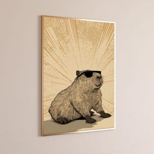May include: A framed wall art print featuring a detailed illustration of a brown capybara wearing black sunglasses. The animal is positioned in the center against a light tan background with radiating lines and a subtle dot pattern effect.
