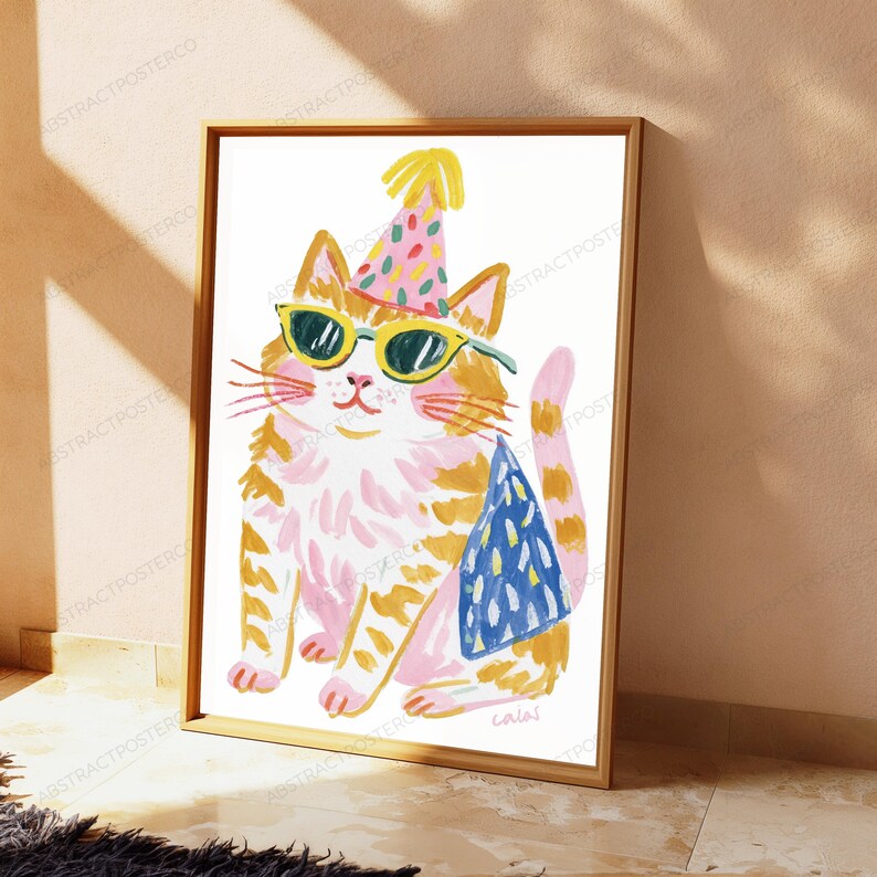 K&ouml;nnte beinhalten: Ein gerahmter Kunstdruck, der eine stilisierte orange-wei&szlig;e getigerte Katze mit einem rosa Partyhut mit buntem Konfettimuster und gelb umrandeter Sonnenbrille zeigt. Die Katze tr&auml;gt einen blau gemusterten Umhang im malerischen Pinselstrichstil.