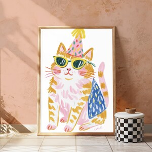 Puede incluir: Una l&aacute;mina enmarcada que muestra un gato atigrado naranja y blanco estilizado con un gorro de fiesta rosa de lunares coloridos y gafas de sol con montura amarilla. El gato lleva una capa azul estampada y tiene una larga cola rosa.
