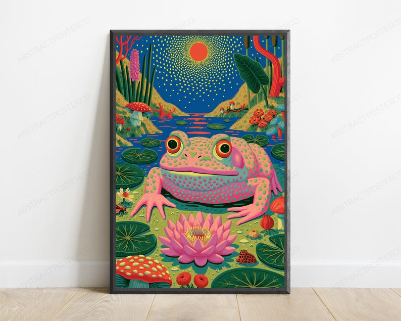 May include: A framed wall art print featuring a vibrant, colorful illustration of a large, pink-spotted frog sitting in a pond. The scene includes a bright pink lotus flower, green lily pads, red mushrooms, and a glowing orange sun in a blue sky.